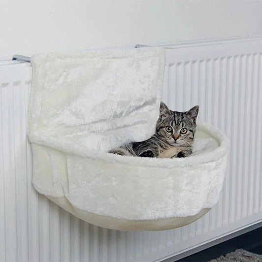 Chat tigré installé dans un cocon en peluche crème suspendu au rebord d'un radiateur blanc — cocon de radiateur pour chat